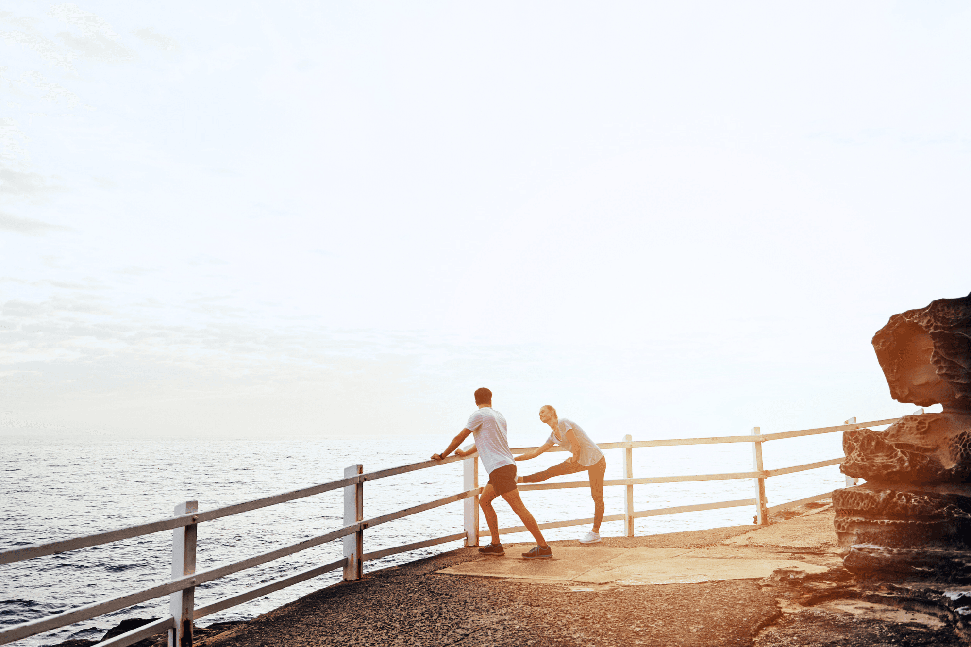 Two people stretching at the seaside at sunset